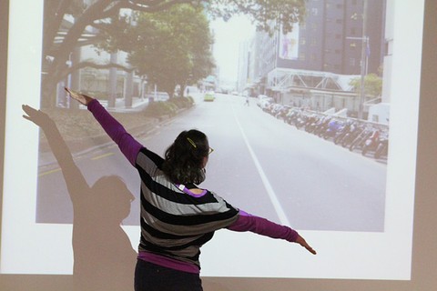 A woman with her arms held wide in front of a projected image of a street.
