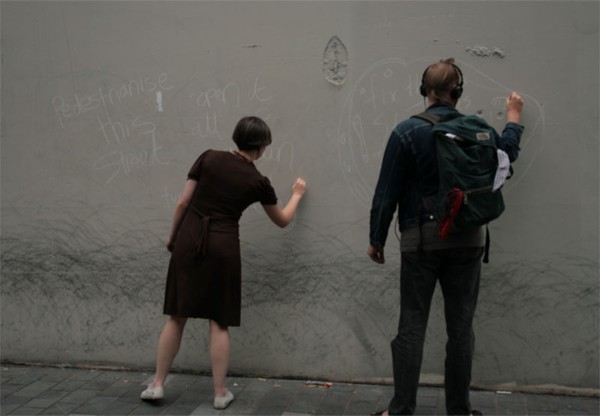 Two people drawing with chalk on a wall.