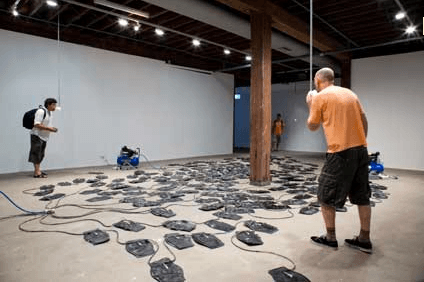 Three man in a room looking at objects on the floor.